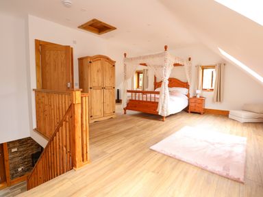 A bedroom with a wooden four-poster bed wardrobe nightstand stair railing and a small carpet at Little Lodge in Pentney near King's Lynn