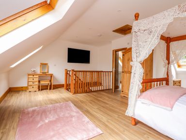 An attic bedroom with a four-poster bed with lace curtains a pink rug wooden furniture and a television on the wall at Little Lodge in Pentney near King s Lynn