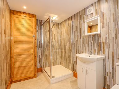 A bathroom with a corner shower enclosure a white sink cabinet a wall mirror and a wooden door at Little Lodge Pentney near King's Lynn