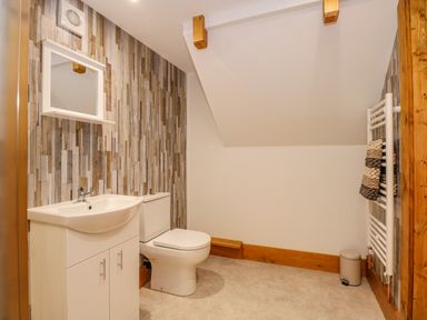A bathroom with a white sink cabinet toilet mirror patterned wall tiles towel radiator and small bin at Little Lodge in Pentney near King's Lynn