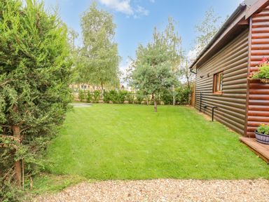 A garden with grass and trees next to a wooden house at Little Lodge in Pentney near King's Lynn