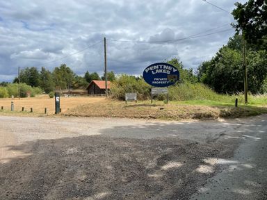 A gravel road intersection with a sign for Pentney Lakes private property near trees and a wooden building at Little Lodge in Pentney near Kings Lynn