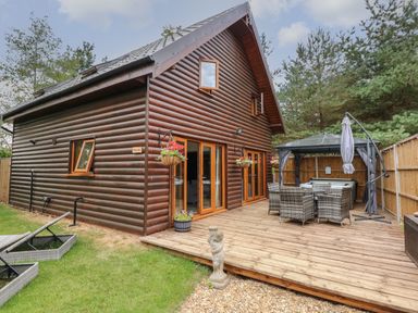 Exterior view of a wooden lodge with a deck patio table chairs gazebo and hanging flower baskets at Little Lodge in Pentney near King's Lynn