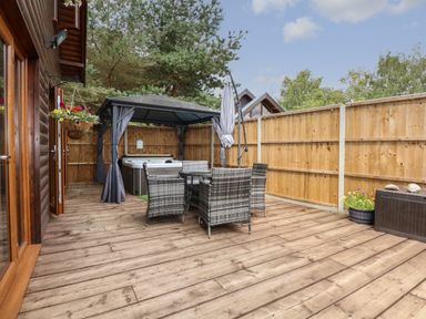 An outdoor wooden deck with wicker chairs and table and a hot tub under a gazebo at Little Lodge in Pentney near Kings Lynn