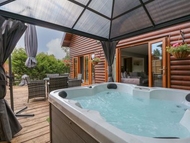 An outdoor deck with a hot tub under a gazebo and a dining table with wicker chairs at Little Lodge in Pentney near Kings Lynn