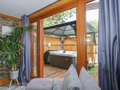 A room with a potted plant and grey curtains looking out through glass doors to a wooden deck with a covered hot tub at Little Lodge in Pentney near King's Lynn