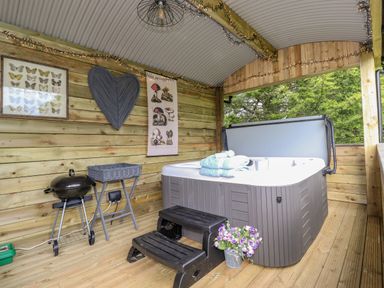 A covered wooden patio with a hot tub steps and a small grill at High Rigg Shepherd's Sunrise in Brampton Cumbria