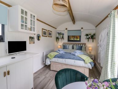 A bedroom with a bed towels and pillows a television on a cabinet and chairs with flowers at High Rigg Shepherd's Sunrise in Brampton Cumbria