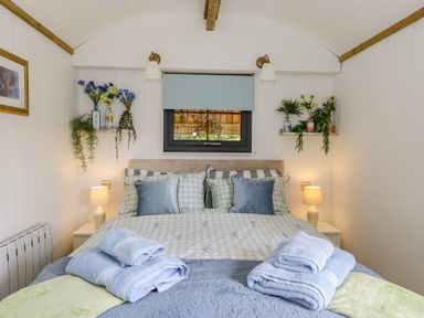 A bedroom with a double bed side tables lamps folded towels flowers on shelves and a small window at High Rigg Shepherd's Sunrise in Brampton Cumbria