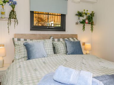 A bedroom with a bed with patterned bedding and two blue pillows with lamps and shelves with flowers on the walls at High Rigg Shepherd's Sunrise in Brampton Cumbria