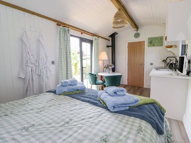 A bedroom with a bed towels robes dining table chairs kitchenette and door at High Rigg Shepherd's Sunrise in Brampton Cumbria