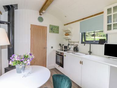 A kitchen with white cabinets and countertop with a built in oven and sink and a round table with flowers and glasses at High Rigg Shepherd's Sunrise in Brampton Cumbria