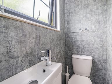A small bathroom with a toilet a sink with a faucet a window and wall cabinets at High Rigg Shepherd's Sunrise in Brampton Cumbria