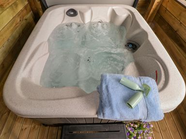 A hot tub with bubbling water and towels with two green glasses on top on a wooden deck at High Rigg Shepherd's Sunrise in Brampton Cumbria