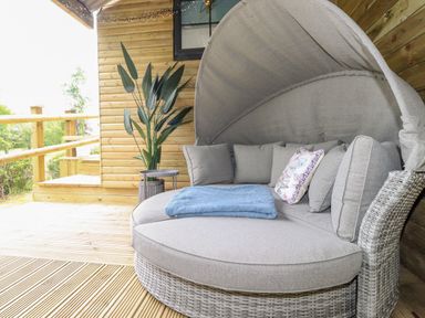 An outdoor seating area with a round cushioned sofa and a potted plant on a wooden deck at High Rigg Shepherd's Sunrise in Brampton Cumbria