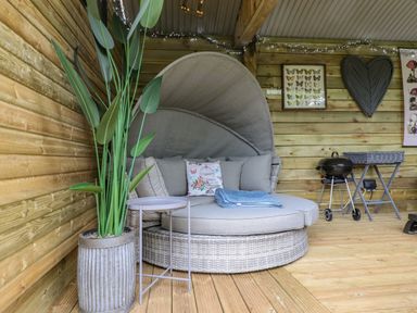 An outdoor seating area with a round cushioned chair a potted plant small table grill and wall decorations at High Rigg Shepherds Sunrise in Brampton Cumbria