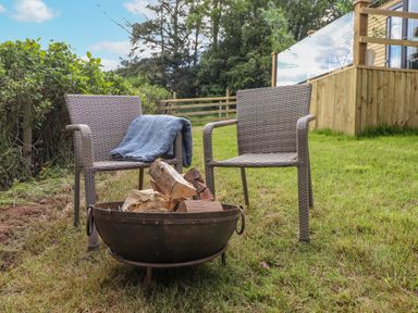 Two outdoor chairs with a blanket and a fire pit with wood in a grassy garden at High Rigg Shepherd's Sunrise in Brampton Cumbria