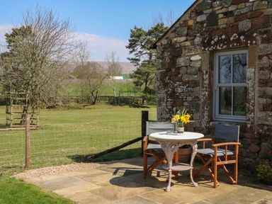 An outdoor stone patio with a small round table and two chairs next to a stone building at Herdie Hideaway in Appleby-In-Westmorland