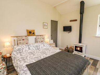 A bedroom with a bed a wood stove a mounted television and a side table at Herdie Hideaway in Appleby-In-Westmorland