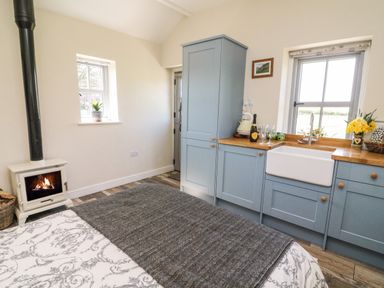 A kitchen area with blue cabinets white sink wood countertop and a burning stove at Herdie Hideaway in Appleby-In-Westmorland