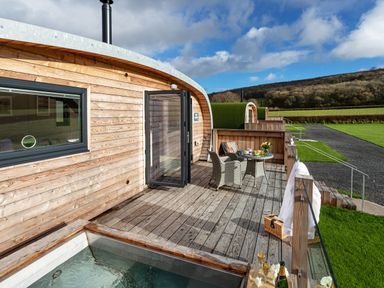 An outdoor wooden deck with a table and two chairs and a hot tub adjacent to a wooden cabin at Middle Longlands in Cartmel