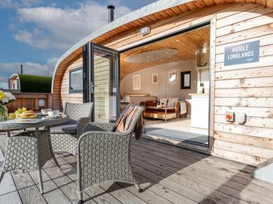 An outdoor seating area with a table and chairs on a wooden deck opening into an indoor living space at Middle Longlands in Cartmel