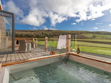 An outdoor wooden deck with a hot tub champagne bottle and glasses and a table with chairs at Middle Longlands in Cartmel