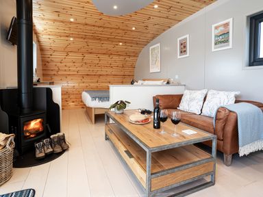 A living room with a brown leather sofa a wooden coffee table with wine glasses and bread and a bed in the background at Middle Longlands in Cartmel