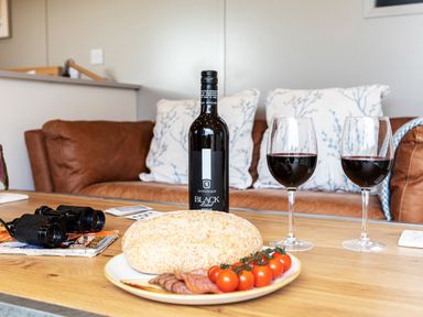 A living room with a bottle of red wine two glasses bread cherry tomatoes and sliced meat on a plate on a wooden table at Middle Longlands in Cartmel