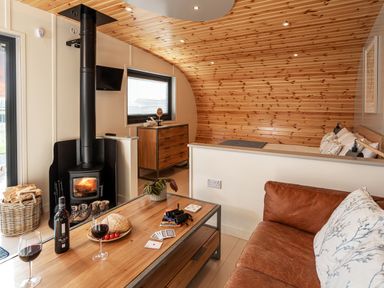 A living room with a wood burning stove sofa coffee table and wooden ceiling at Middle Longlands in Cartmel