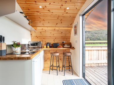 A small kitchen with wooden walls and ceiling two stools at a counter and a door opening to a deck at Middle Longlands in Cartmel