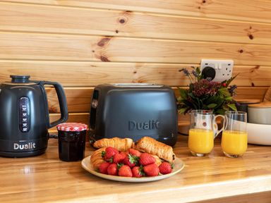 A kitchen counter with a black kettle and toaster a plate of croissants and strawberries two glasses of orange juice and a flower vase at Middle Longlands in Cartmel