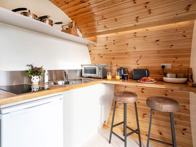 A small kitchen with wooden walls two stools a sink a toaster a kettle and a plate of food at Middle Longlands in Cartmel