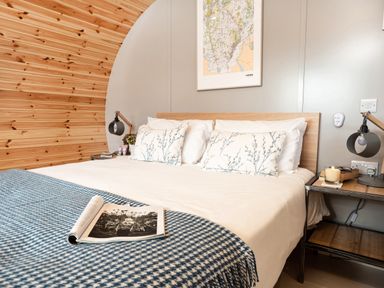 A bedroom with a bed with white linens and blue patterned pillows an open book on a blue checkered blanket wood paneling and a framed map on the wall at Middle Longlands in Cartmel