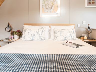 A bed with patterned pillows and a checkered blanket with bedside tables and lamps at Middle Longlands in Cartmel