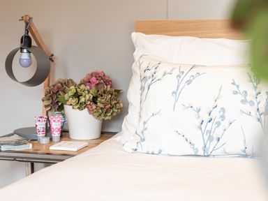 A bed with a floral pillow and a wooden headboard next to a bedside table with a lamp flower pot and toiletries at Middle Longlands in Cartmel