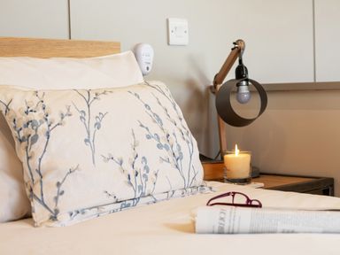A bed with a pillow and white sheets next to a bedside table with a lamp and candle at Middle Longlands in Cartmel