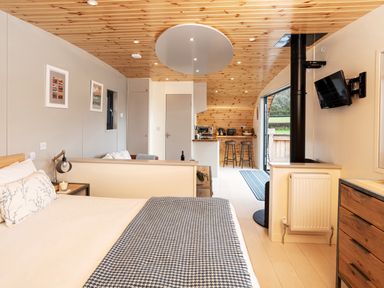A bedroom with a bed a kitchen bar stools and a mounted television at Middle Longlands in Cartmel