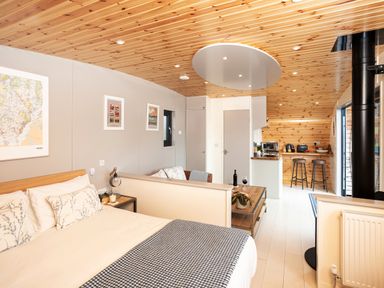 An open studio layout with a bed a small sofa a coffee table a kitchen area with bar stools and wooden ceiling at Middle Longlands in Cartmel