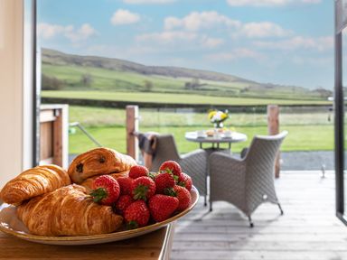 A plate with croissants and strawberries on a counter overlooking a patio with chairs and a table at Middle Longlands in Cartmel