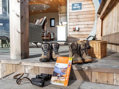 Hiking boots binoculars and a map on a wooden deck outside a cabin at Middle Longlands in Cartmel
