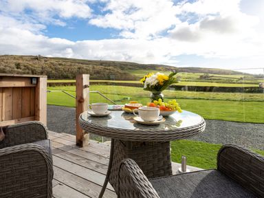 An outdoor patio with a glass table and wicker chairs overlooking green fields at Middle Longlands in Cartmel