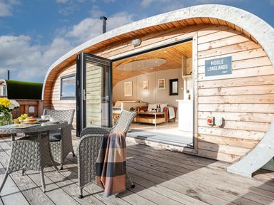 An outdoor patio with a table and chairs outside a wooden cabin with an open door at Middle Longlands in Cartmel