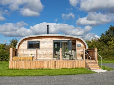 A curved wooden cabin with a front porch, chairs and table outside at High Longlands in Cartmel