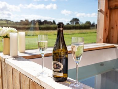 A bottle of prosecco with two glasses of water on the edge of a wooden hot tub at High Longlands in Cartmel