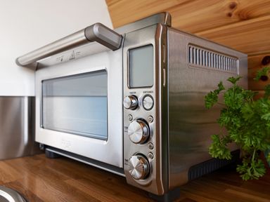 A stainless steel toaster oven with control knobs on a wooden countertop with green parsley beside it at High Longlands in Cartmel