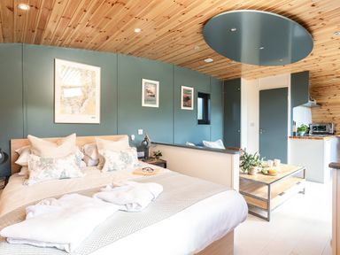A bedroom with a double bed pillows and robes a coffee table with cups and plants and a kitchenette area at High Longlands in Cartmel