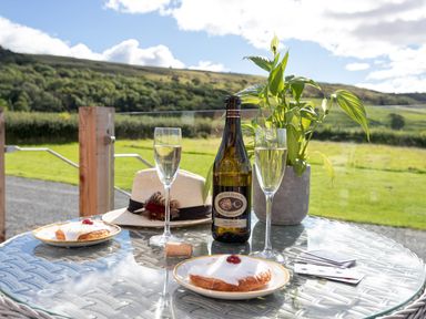 An outdoor table with prosecco bottle two glasses pastries playing cards and a plant at High Longlands in Cartmel