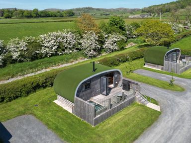Two cabins with grass roofs and wooden exteriors in a green outdoor area at High Longlands in Cartmel