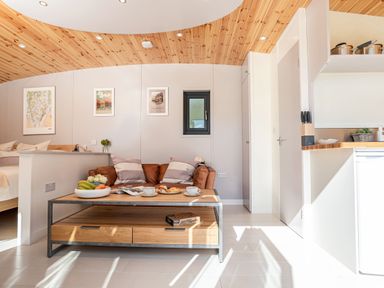 A living area with a brown sofa and coffee table next to a bed and kitchen at Little Heaning in Cartmel